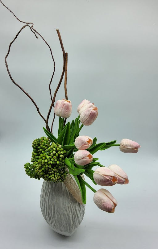 White vase filled with pink tulips, green cactus and brown twigs